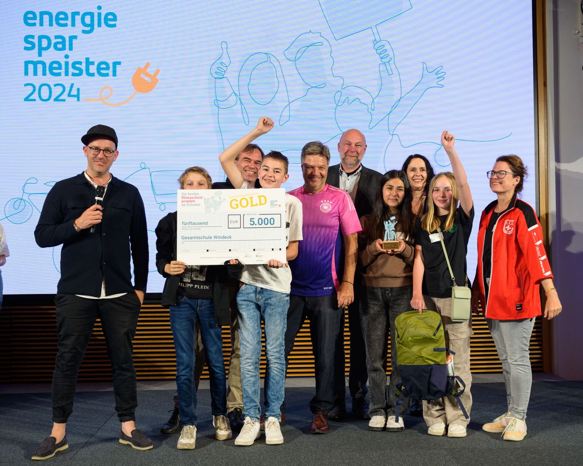 Foto ©co2online / Phil Dera - v. l.: Die Mitglieder der Schülergenossenschaft mit Wirtschaftsminister Robert Habeck im Deutschlandtrikot, daneben Holger Siems und Elisabeth Winkelmeier-Becker, MdB